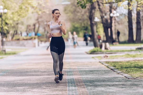 Attractive sportswoman jogging along wide alley in green park — Stock Photo