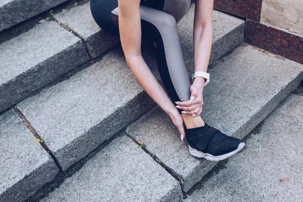 Schuss auf Sportlerin, die auf Treppe sitzt und verletztes Bein berührt — Stockfoto