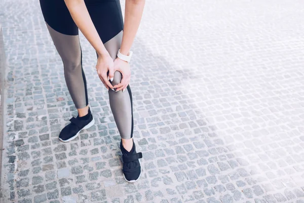 Partial view of injured sportswoman standing on pavement and touching knee — Stock Photo