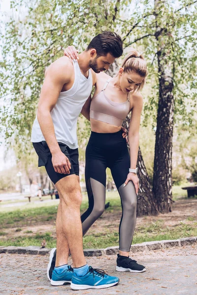 Young sportswoman with injured leg walking while supported by handsome sportsman — Stock Photo