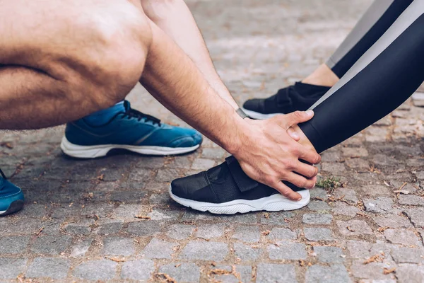 Cropped shot of sportsman touching injured leg of sportswoman in sneakers — Stock Photo