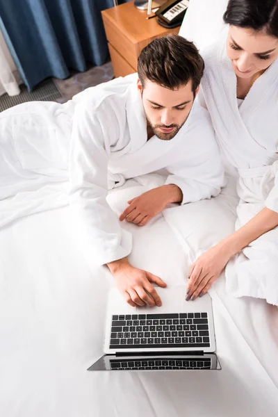 Vue de dessus de l'homme barbu utilisant l'ordinateur portable près de femme attrayante dans la chambre d'hôtel — Photo de stock