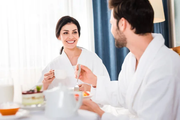 Enfoque selectivo de la mujer feliz con la taza mirando al hombre barbudo tenedor de celebración - foto de stock