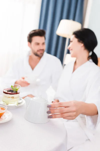 Selective focus of woman holding teapot and looking at man — Stock Photo