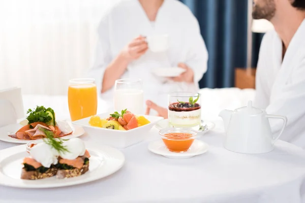 Селективный фокус вкусного завтрака на столе рядом с мужчиной и женщиной — стоковое фото