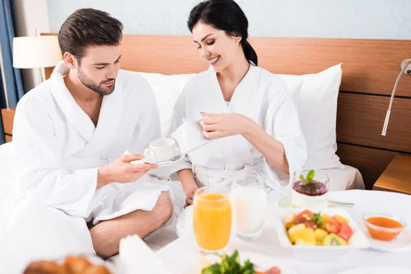 Feliz mujer sosteniendo té olla cerca barbudo hombre con taza — Stock Photo