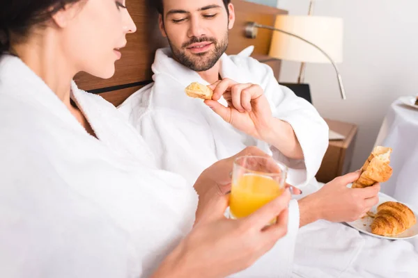 Foco seletivo do homem segurando croissant perto de mulher atraente com vidro de suco de laranja — Fotografia de Stock
