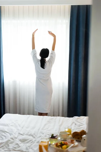 Vista posteriore di donna bruna in piedi con le mani tese in camera d'albergo — Foto stock