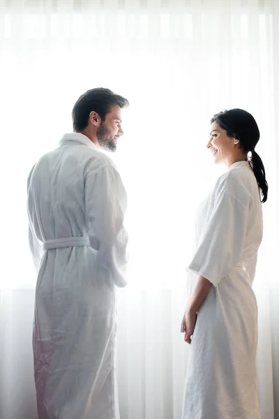 Low angle view of happy man and attractive woman in bathrobes standing and looking at each other — Stock Photo