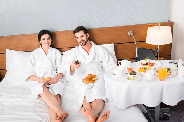 Homme gai tenant télécommande près de la femme avec un verre de jus d'orange — Photo de stock