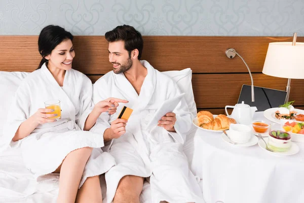 Donna felice che punta con il dito a colazione vicino all'uomo con carta di credito e tablet digitale — Foto stock