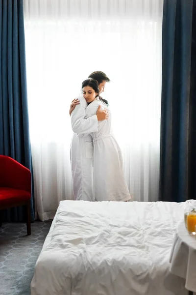 Hombre guapo y hermosa mujer abrazándose en la habitación de hotel - foto de stock