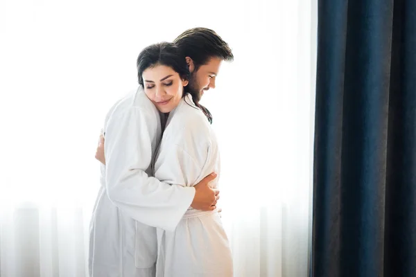 Homem barbudo alegre abraçando mulher atraente no quarto de hotel — Fotografia de Stock