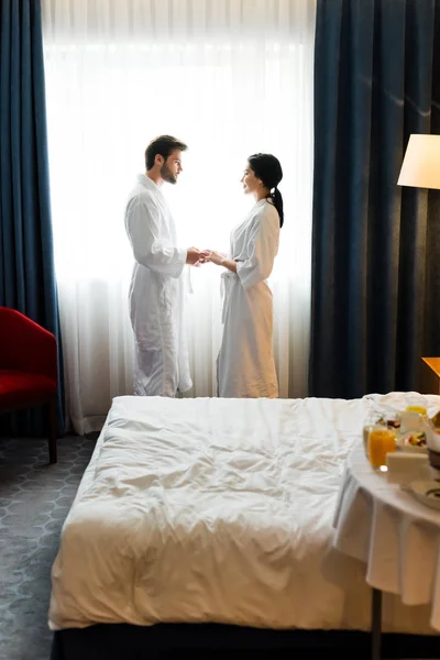 Selective focus of handsome bearded man holding hands with attractive woman in hotel room — Stock Photo