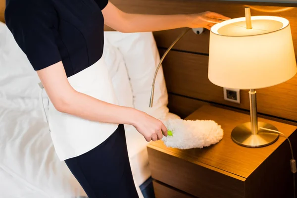 Cropped view of housemaid in white apron holding duster and cleaning hotel room — Stock Photo