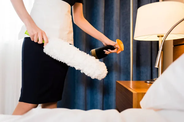 Горничная в форме держит пыльник и бутылку во время уборки гостиничного номера — стоковое фото