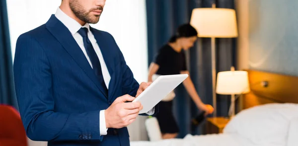 Tiro panorâmico do homem usando tablet digital perto da empregada doméstica no quarto do hotel — Fotografia de Stock