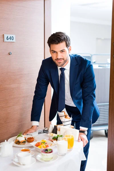 Selektiver Fokus der glücklichen Empfangsdame, die das Frühstück auf dem Speisewagen des Hotels bringt — Stockfoto