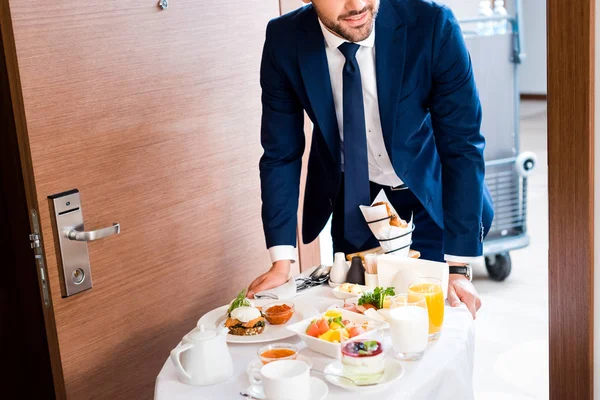 Vista recortada de la recepcionista que trae el desayuno en el carrito de comida del hotel - foto de stock