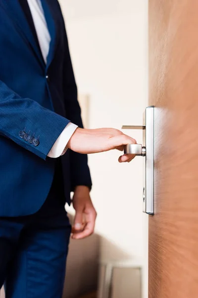 Vista recortada del hombre de pie cerca de la puerta y tocar la manija de la puerta - foto de stock