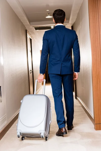 Rückansicht des Geschäftsmannes, der mit Koffer im Hotelflur spaziert — Stockfoto