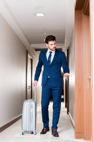 Guapo hombre de negocios sosteniendo tarjeta de hotel mientras está de pie con la maleta - foto de stock