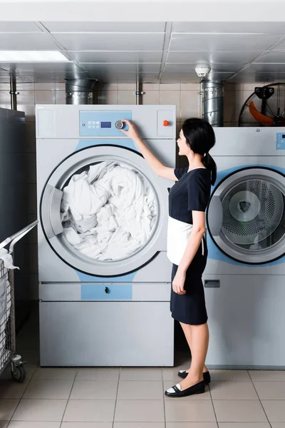 Brunette maid standing and touching button on washing machine in laundry — Stock Photo