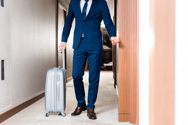 Обрезанный вид бизнесмена с гостиничной картой, стоящего рядом с чемоданом — стоковое фото