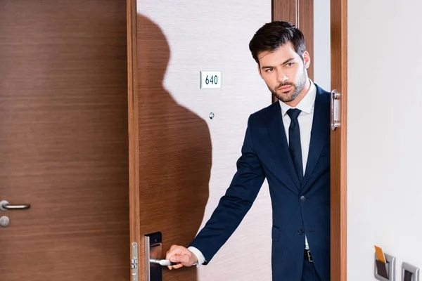 Hombre de negocios guapo y barbudo en traje que entra en la habitación del hotel - foto de stock