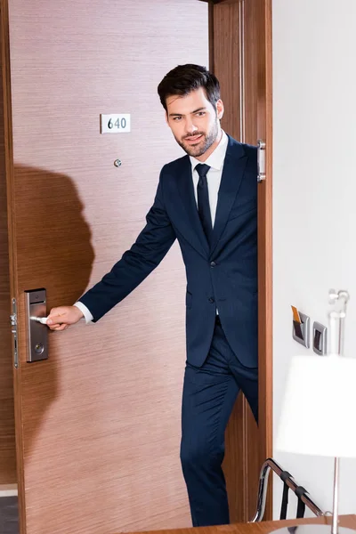 Hombre de negocios alegre y barbudo en traje que entra en la habitación del hotel - foto de stock