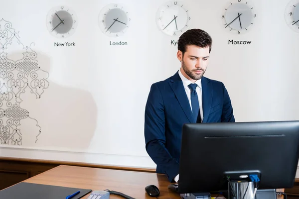 Handsome receptionist in suit looking at computer monitor in hotel — Stock Photo