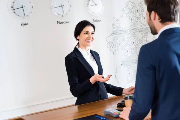 Selektiver Fokus der glücklichen Empfangsdame, die gestikuliert, während sie den Mann ansieht — Stockfoto