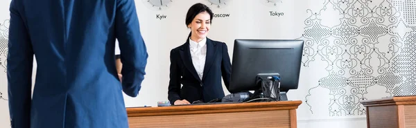Tiro panorâmico de homem de negócios perto de recepcionista alegre olhando para monitor de computador — Fotografia de Stock