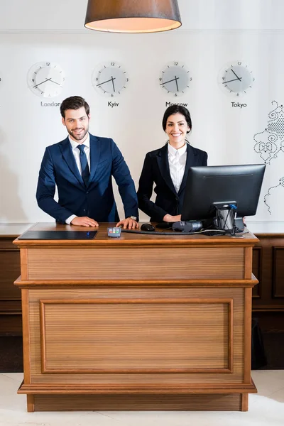 Cheerful receptionists in formal wear standing at reception desk — Stock Photo