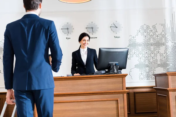 Vista trasera del hombre de negocios cerca de la recepcionista alegre mirando el monitor de la computadora - foto de stock