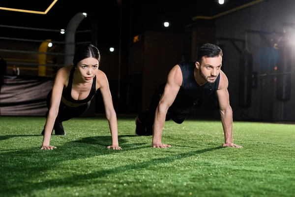 Serious woman doing plank exercise near handsome man on grass — Stock Photo