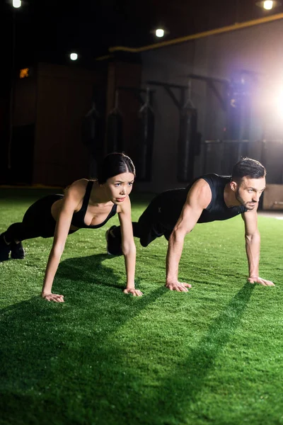 Sérieux femme faire planche exercice près barbu homme sur herbe verte — Photo de stock