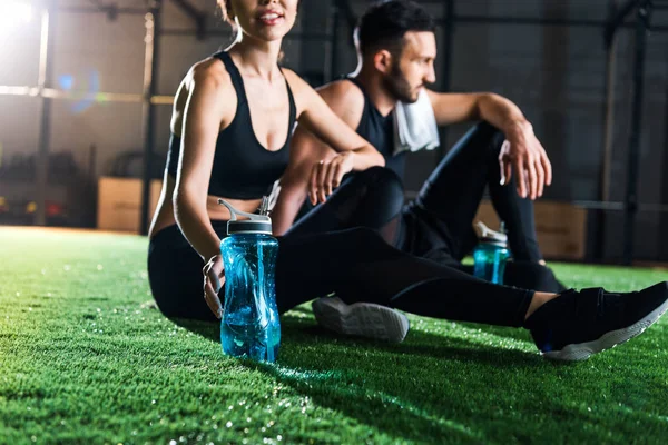 Vue recadrée de femme heureuse assise près de l'homme et tenant bouteille de sport — Photo de stock