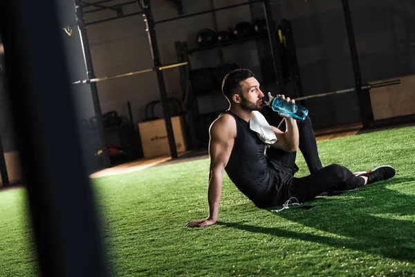 Selective focus of man in sportswear drinking water while sitting on grass — Stock Photo