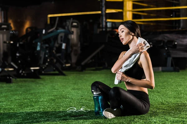 Mujer atlética sosteniendo la toalla mientras está sentado con las piernas cruzadas en la hierba - foto de stock