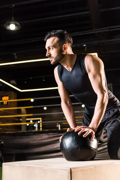 Blick aus dem niedrigen Winkel auf einen ernsten Mann, der in der Nähe einer Kniebeuge steht und Ball hält — Stockfoto