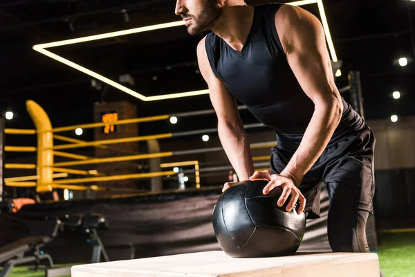 Cropped view of serious man holding ball while standing near squat box — Stock Photo