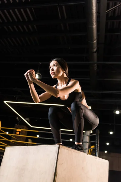 Visão de baixo ângulo da mulher atraente fazendo exercício agachamento na caixa de agachamento — Fotografia de Stock