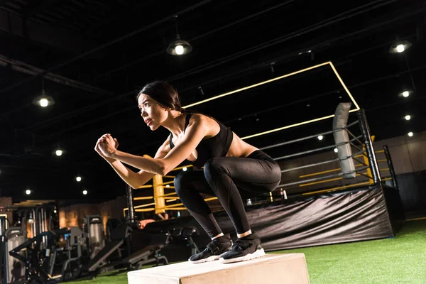 Vista basso angolo di donna attraente che fa esercizio squat su scatola tozza in palestra — Foto stock