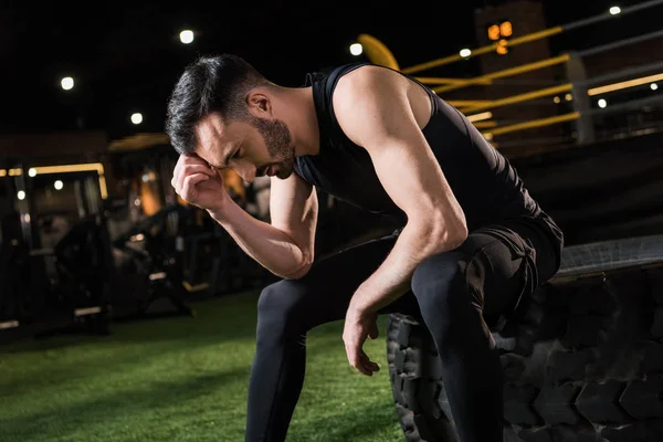 Handsome and tired athletic man sitting on car tire in gym — Stock Photo