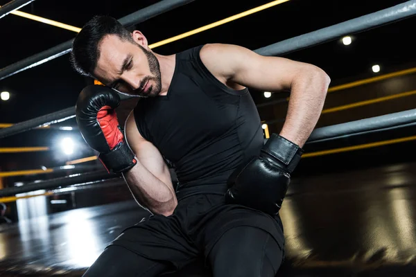 Low angle view of tired bearded man in black boxing gloves touching head in gym — Stock Photo