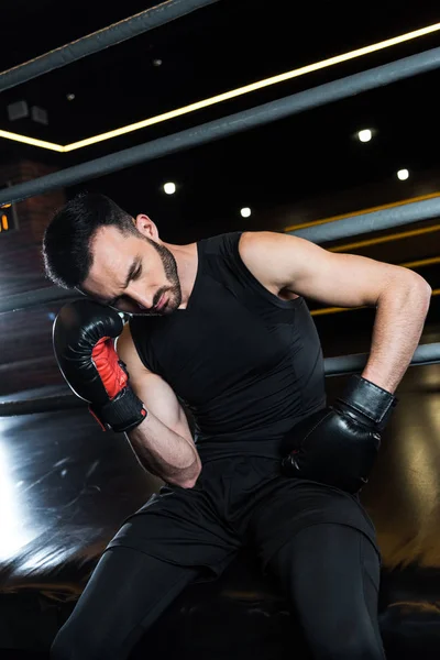 Low angle view of exhausted bearded man in black boxing gloves touching head in gym — Stock Photo