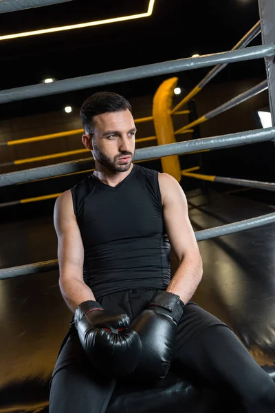 Müder bärtiger Mann in schwarzen Boxhandschuhen sitzt im Fitnessstudio — Stockfoto