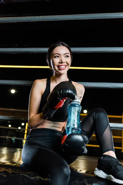 Низкий угол зрения веселой женщины в боксёрских перчатках, держащей спортивную бутылку — стоковое фото