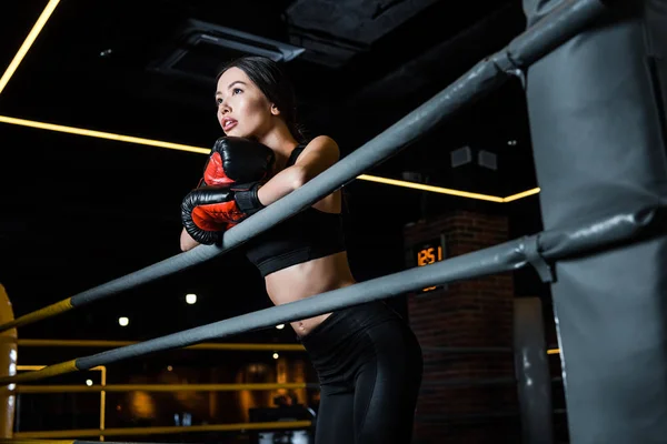 Vue à faible angle de la femme attrayante dans des gants de boxe debout dans le centre sportif — Photo de stock